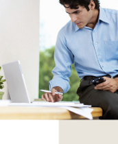 A man sits at a desk with his blackberry and review information on his laptop computer.