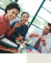 Three business people sitting at a table in a sunny boardroom, smiling and talking.